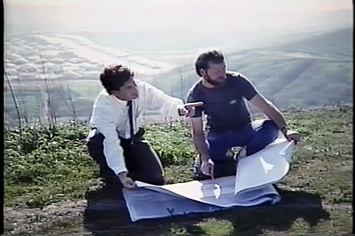 Two men are sitting on a hill looking at plans.